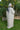 Woman in a white abaya standing in a garden with greenery and hanging lights.