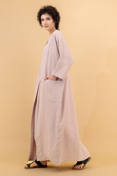 A woman modeling a long, loose-fitting abaya in a light blush pink color.